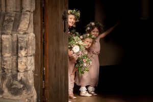 Flower girls peeking out from behind the large church door