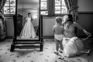 The bride looking in the mirror while her flower girl gets dressed